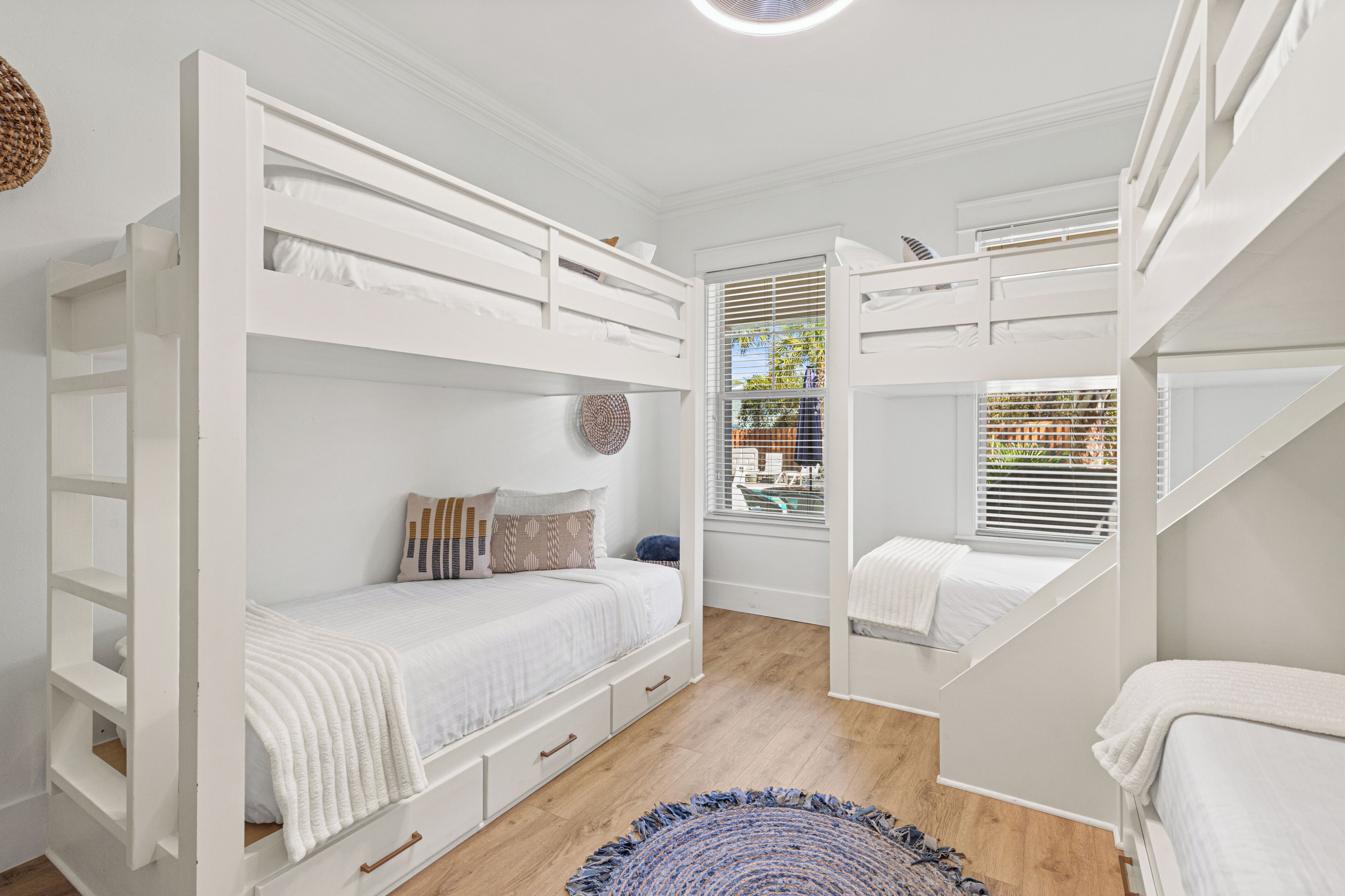 Una habitación con literas, una ventana con persianas y una alfombra de fibras naturales.