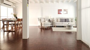 A spacious living room with a wooden floor, a dining area with a table and chairs, a white sofa, and a coffee table.