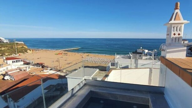 A coastal view from a balcony overlooking a beach, a white tower, and a clear blue sky.