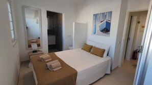 A hotel room with a bed, a bedside table with towels, a mirror, and a painting on the wall.