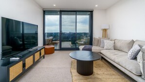 Una sala de estar moderna con un televisor de pantalla plana grande, un sofá, una mesa de centro y vistas a través de una puerta corrediza de vidrio.