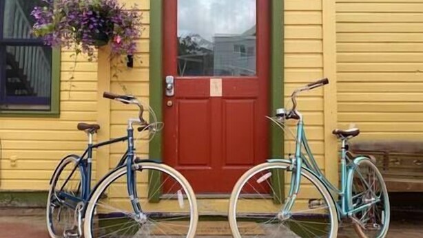 Two bicycles parked in front of a yellow building with a red door. - Petite Maison: Hip & Historic (Telluride)
