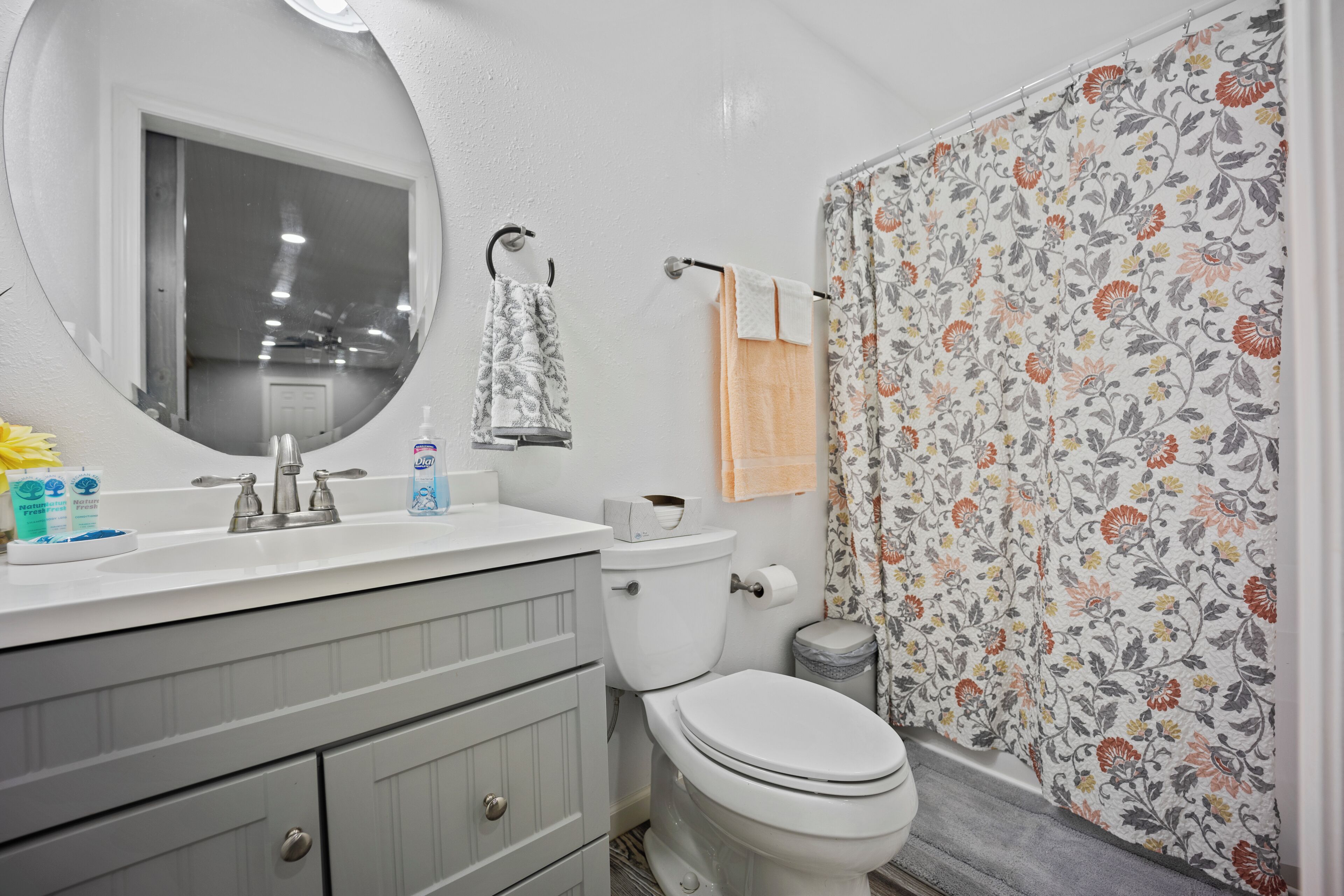 Un bany amb un vàter blanc, un lavabo amb un mirall a sobre i una cortina de bany amb un dibuix floral.