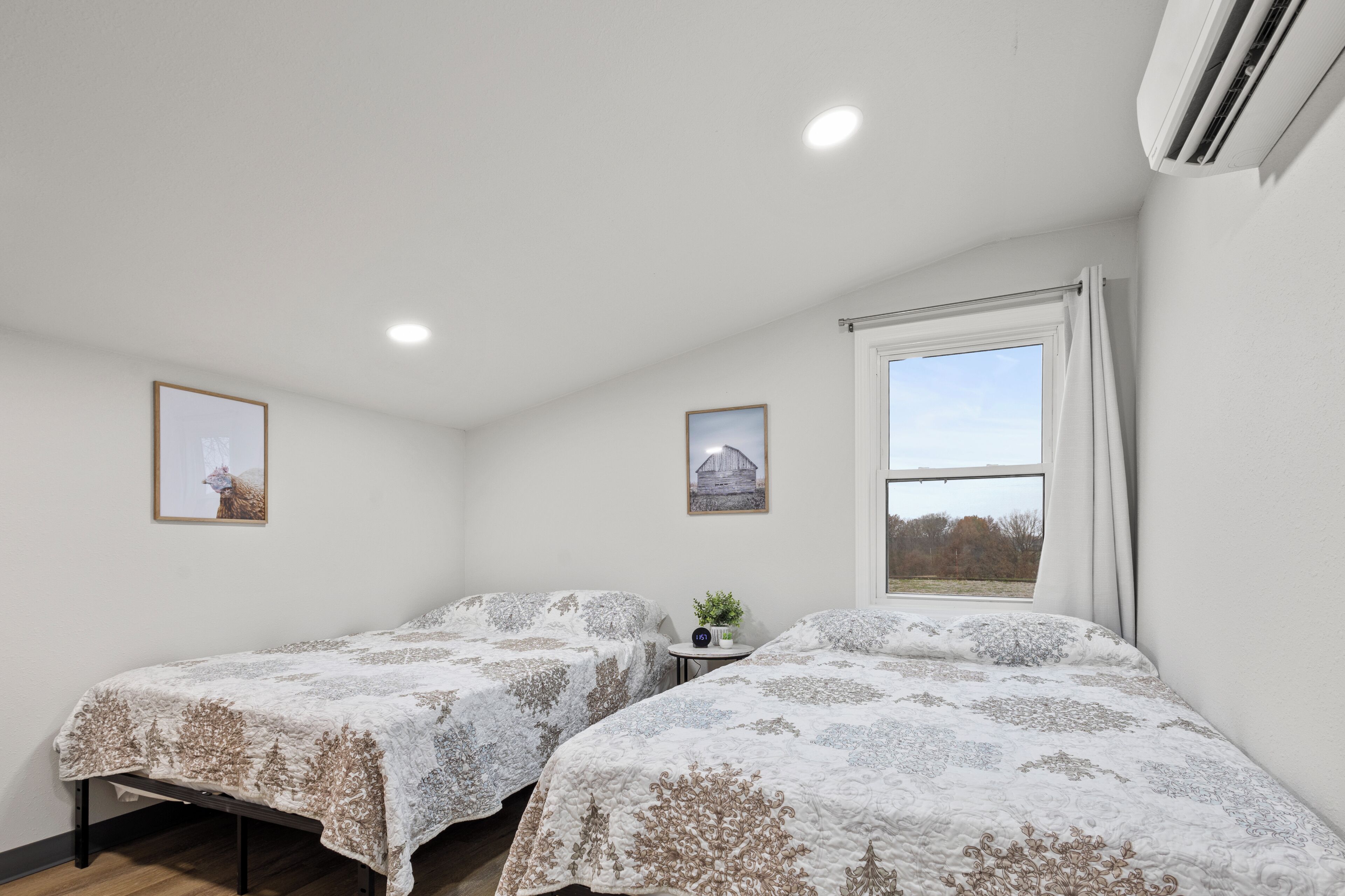 Une chambre avec deux lits, une petite table sur laquelle est posée une plante, et deux tableaux encadrés accrochés au mur.