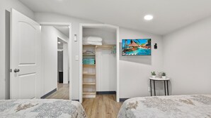 Une chambre avec deux lits, une armoire avec des étagères, un tableau au mur et une petite table avec des plantes.