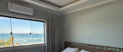 A hotel room with a bed, a nightstand, a window with a view of the ocean, and an air conditioning unit.