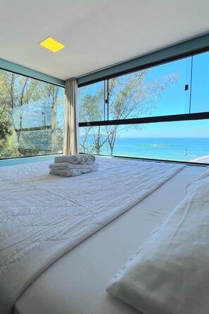 A bedroom with a large bed, a view of the sea, and a skylight. - Graffi Beach Houses (Florianópolis)