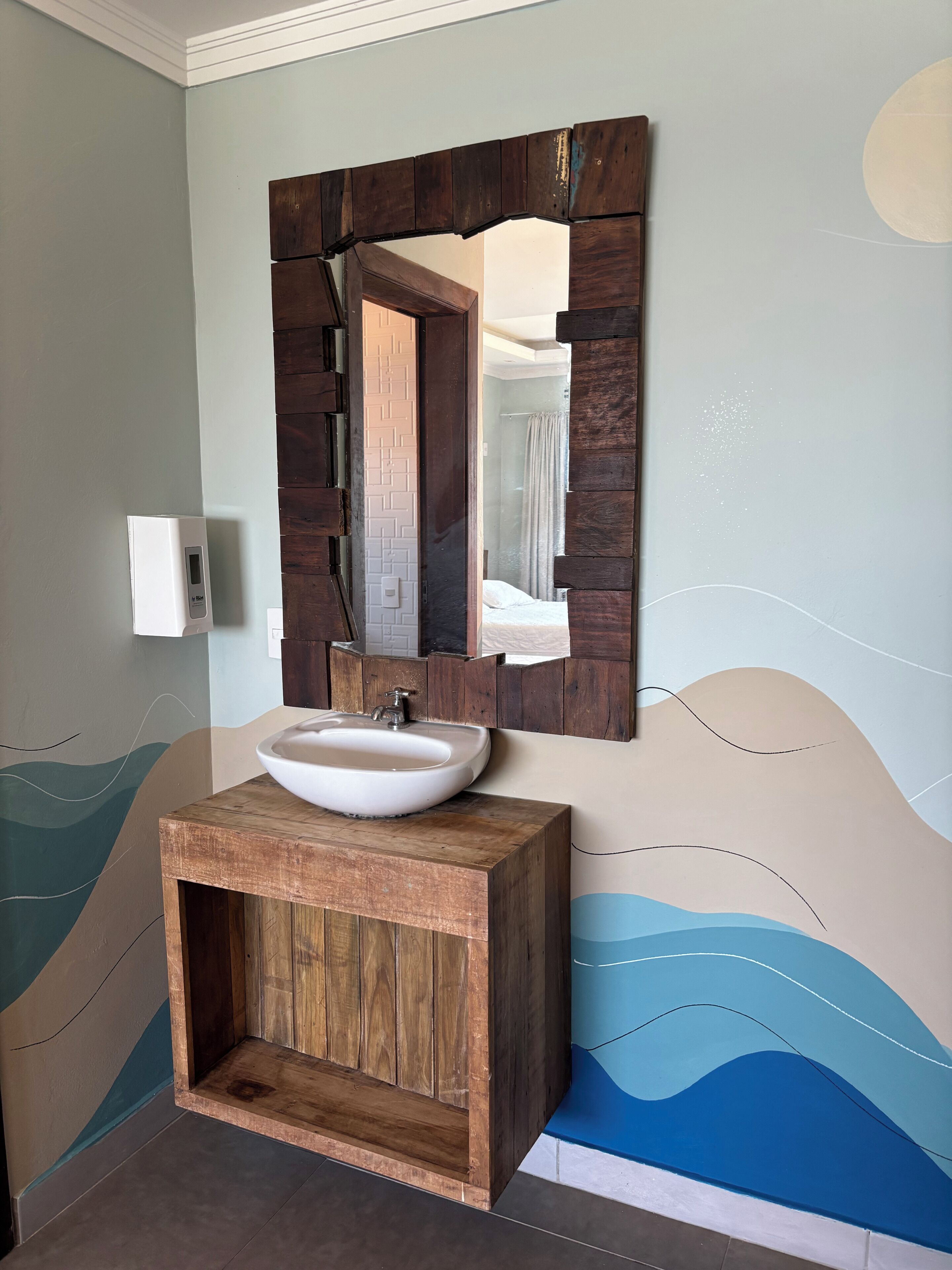A bathroom with a wooden vanity, a white sink, and a mirror with a wooden frame.