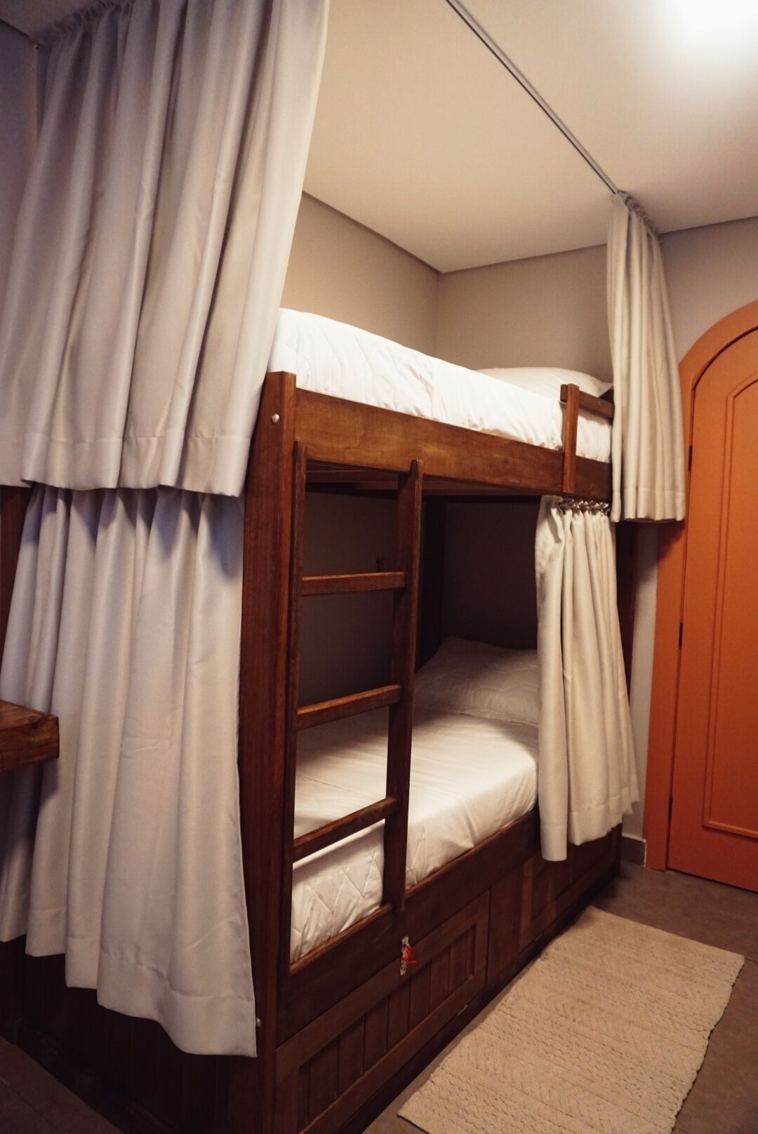 A bunk bed with white bedding and curtains, a wooden floor, and a door in the background.