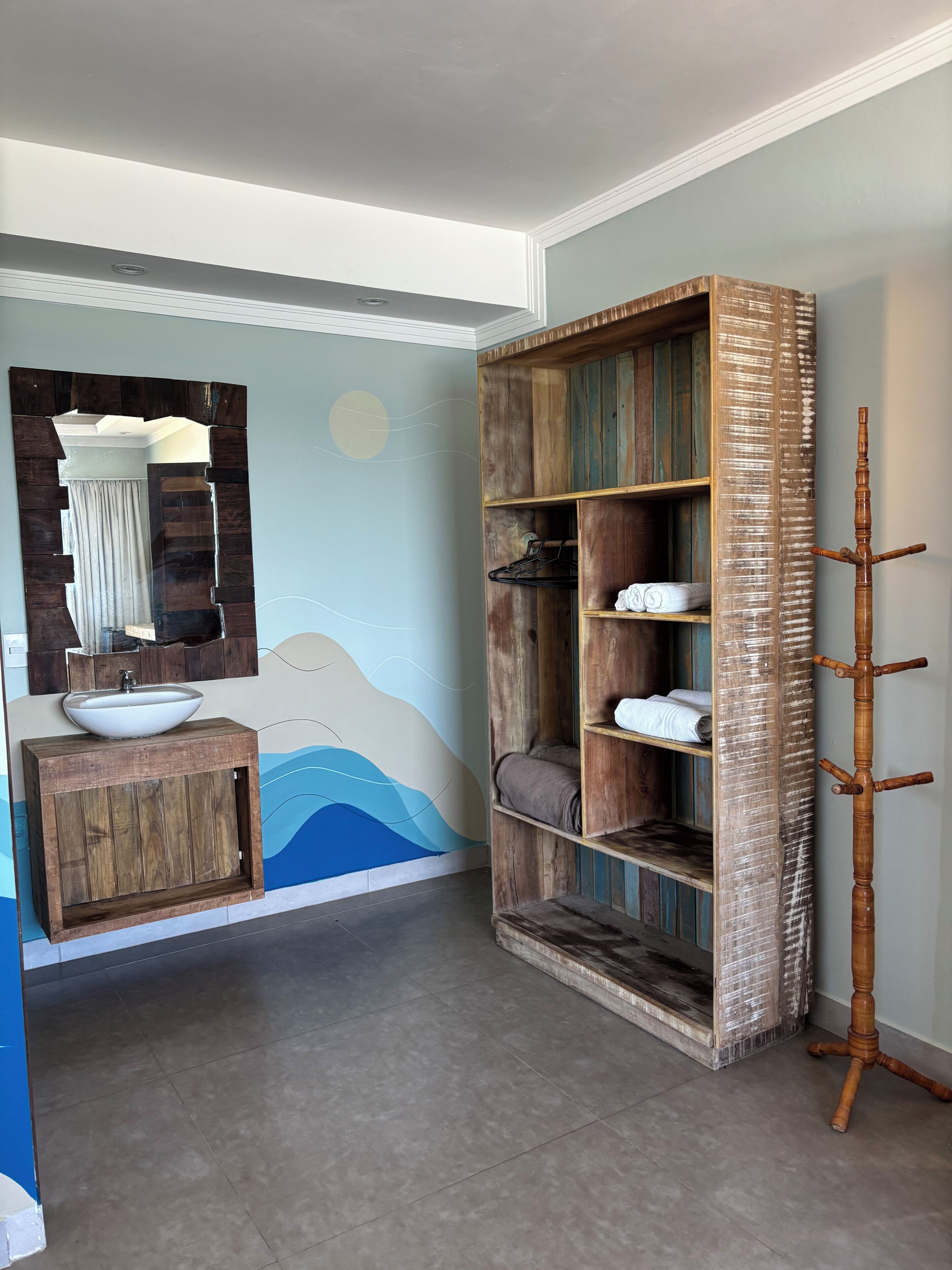A bathroom with a wooden vanity, a large mirror, and a wall-mounted shelf with towels.