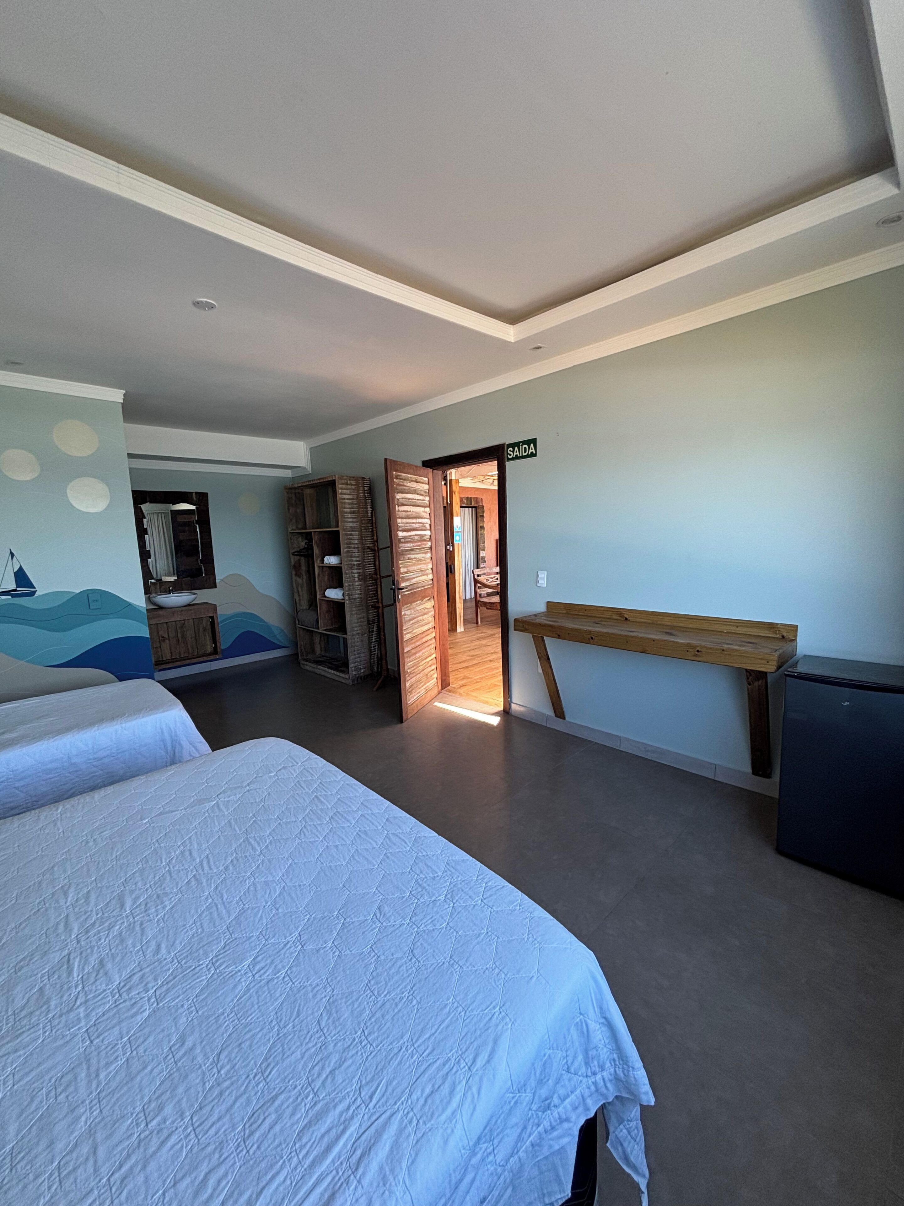 A bedroom with two beds, a wooden bench, a small table, and a wall with a nautical mural.