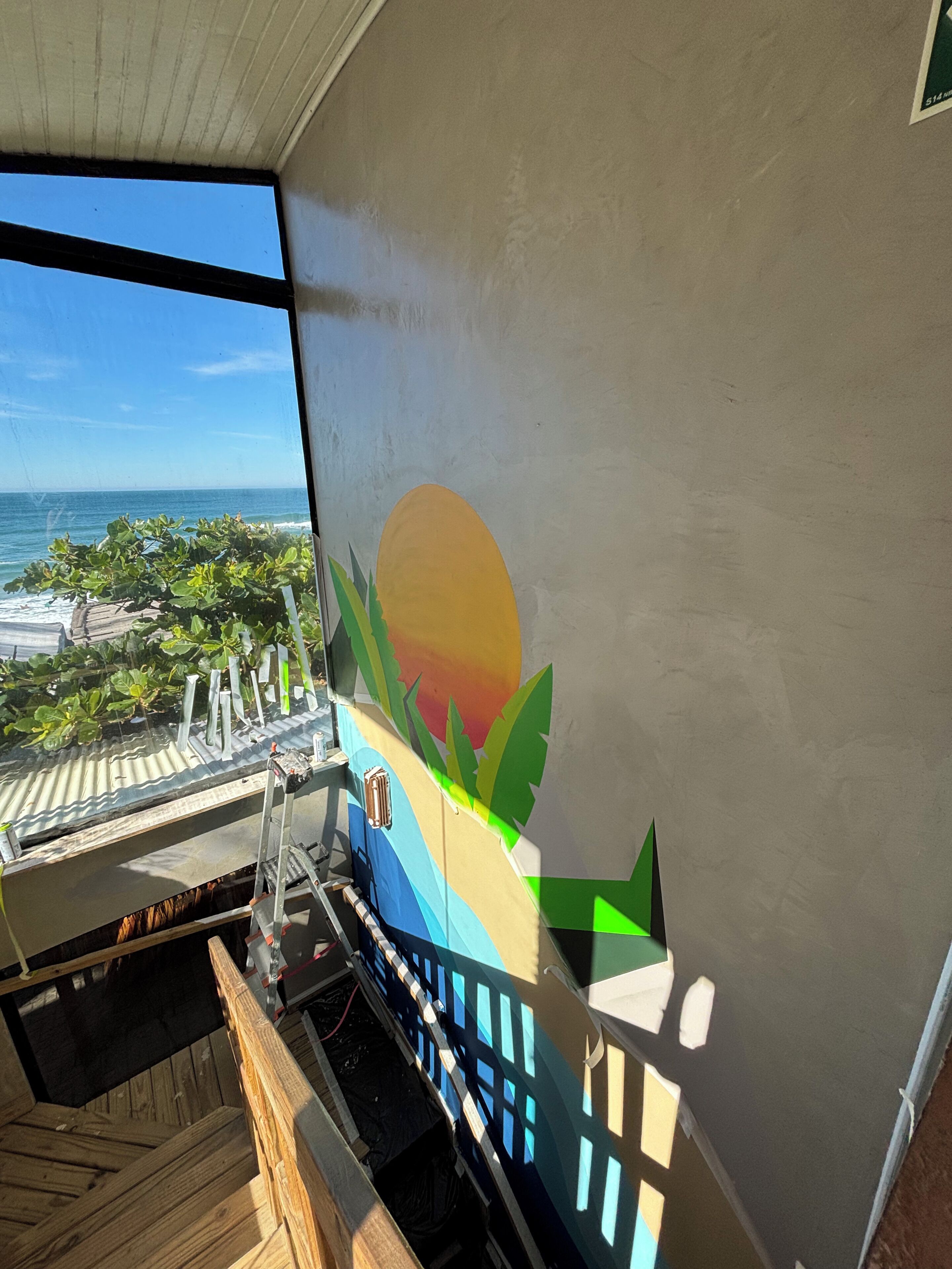 Una habitación con vista al océano, una terraza de madera y un mural colorido en la pared.