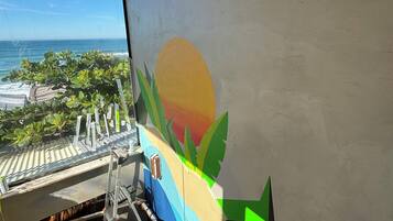 Una habitación con vista al océano, una terraza de madera y un mural colorido en la pared.