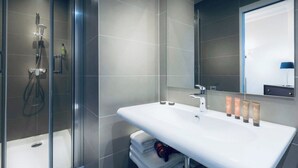 A modern bathroom with a glass-enclosed shower, a white sink with multiple toiletries, and a large mirror.