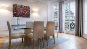A modern dining area with a glass table, four chairs, and a colorful abstract painting on the wall.