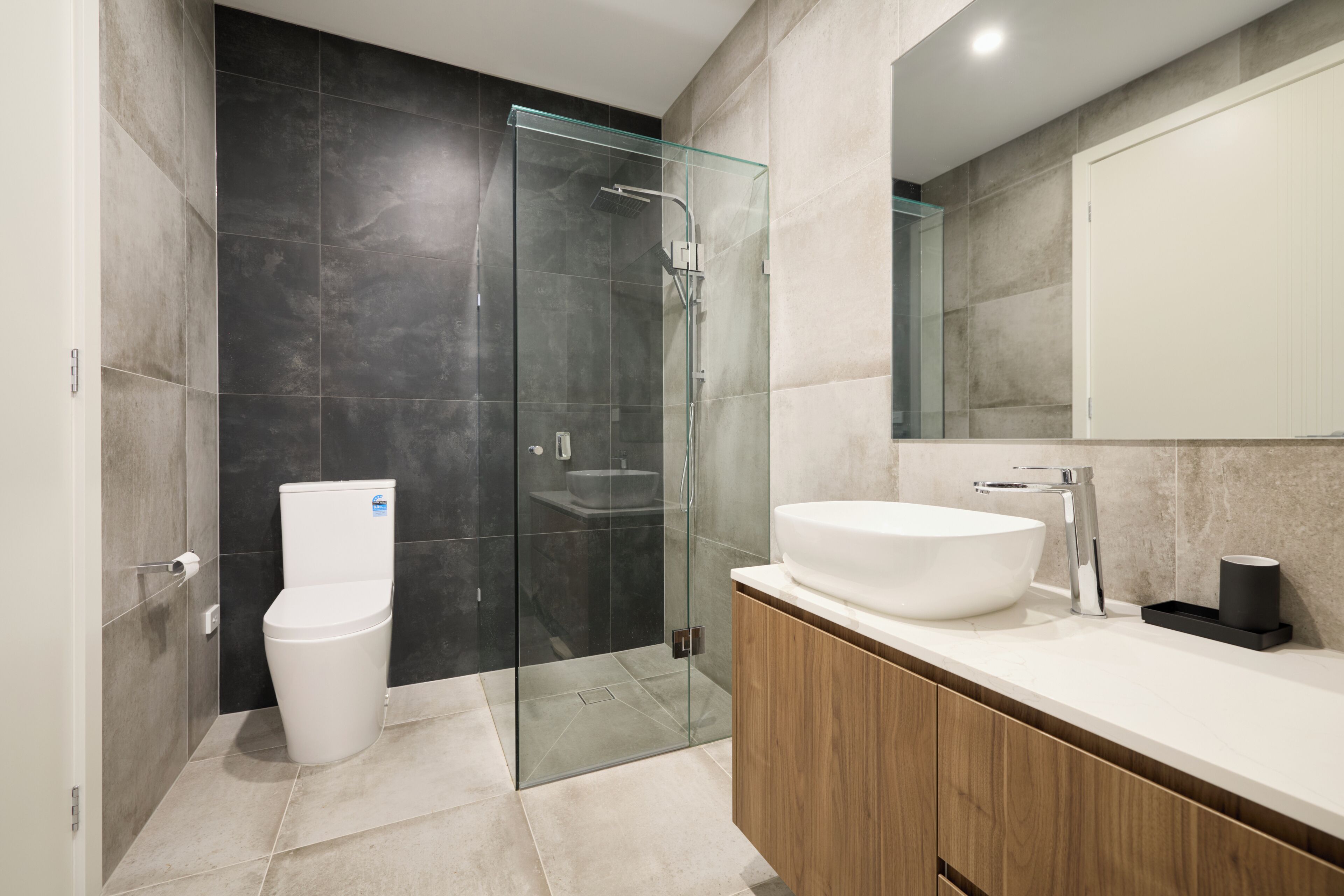 Un bagno moderno con cabina doccia in vetro, un WC bianco, un mobile lavabo in legno e uno specchio grande.
