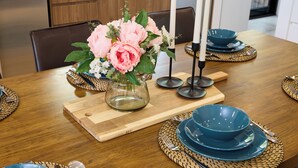 Ein Holztisch mit blauen Tellern, einer Vase mit rosa Blumen und Kerzen.