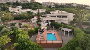 Ein modernes Gebäude mit Pool auf dem Dach, umgeben von üppiger Vegetation und freiem Blick auf eine Hügelstadt.
