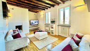 A modern living room with a wooden ceiling, white sofas, a television, and a fireplace. - Vetrina Roma - Stay in Luxury (Roma)