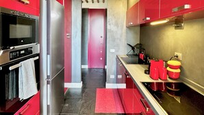 A modern kitchen with red cabinets, stainless steel appliances, and a wooden ceiling. - Vetrina Roma - Stay in Luxury (Roma)