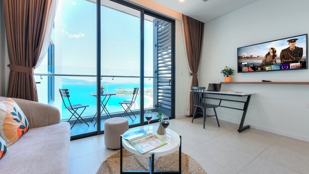Un salon moderne avec un balcon donnant sur un paysage magnifique, un téléviseur à écran plat fixé au mur et un coin repas avec une table et des chaises.