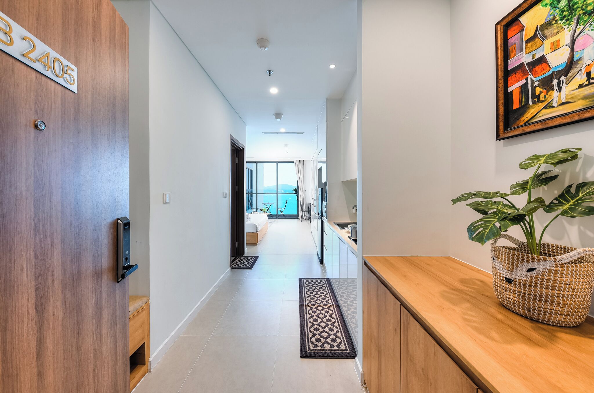 A modern hallway with a wooden door labeled "32405," a reception area with a woven basket, and a view of a room with a large window.