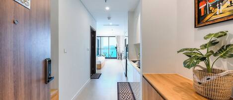 A modern hallway with a wooden door labeled "32405," a reception area with a woven basket, and a view of a room with a large window.