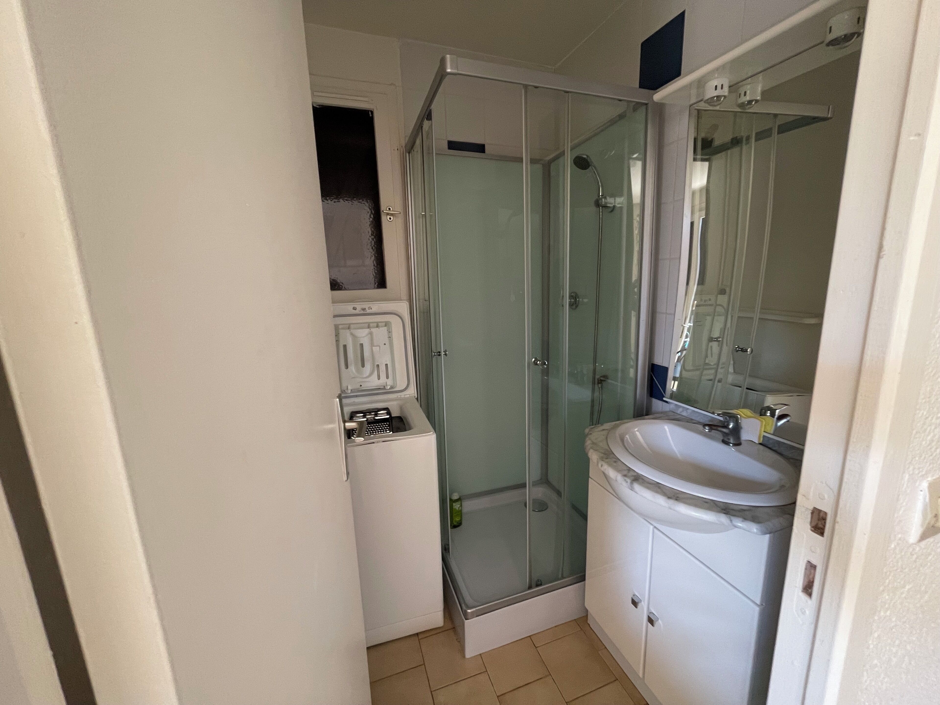 Une salle de bain compacte avec une douche à parois de verre, un lavabo blanc et un petit meuble de rangement.