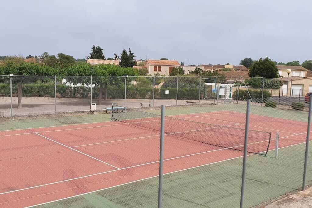 Ein Tennisplatz mit Netz, umgeben von einem Maschendrahtzaun, mit Häusern im Hintergrund.