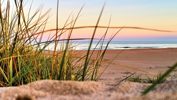 A beach with sand and grass in the foreground.