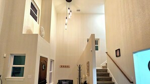 A spacious hallway with a wooden floor, a staircase, and a ceiling with a unique design.