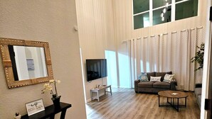 A spacious living room with a wooden floor, a black console table, a sofa, and a TV.