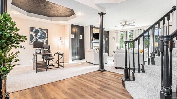 A spacious living area with a wooden floor, a staircase with black railings, and a modern kitchen in the background. - Executive Rental 5BR 5BA, Arcade, Bounce House, GYM, Grill (Omaha)