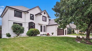 A two-story house with a front lawn, a driveway, and a garage. - Executive Rental 5BR 5BA, Arcade, Bounce House, GYM, Grill (Omaha)