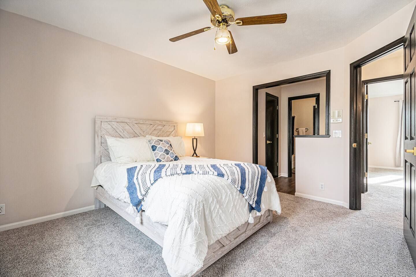 A bedroom with a bed, a ceiling fan, a nightstand, and a door leading to another room.