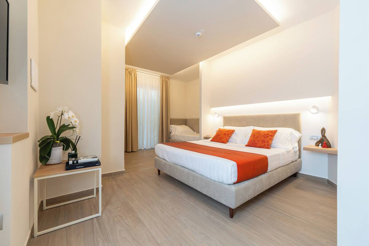 A modern hotel room with a large bed, a bedside table, and a potted plant.