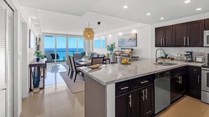 A modern kitchen with dark cabinets, a large island, and a view to the outside. - Serena Beachfront 2 BRS Direct OceanView w Parking (Miami Beach)