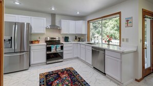 Une cuisine moderne avec des meubles blancs, des appareils en acier inoxydable et une grande fenêtre donnant sur un paysage verdoyant.