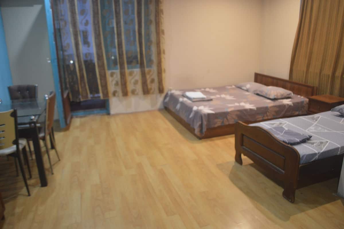 A room with two wooden beds, a dining table with chairs, and a window with curtains.