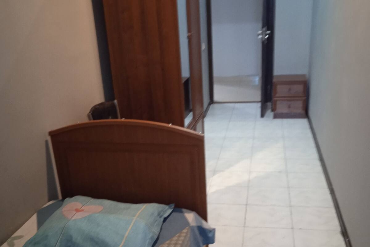 A narrow hallway with a bed on the left, a wooden wardrobe, and a door at the end.