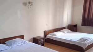 A hotel room with two beds, wooden flooring, and a small bedside table with a lamp. - sunshine (Batumi)