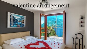 A bedroom with a bed, a heart-shaped rose arrangement on the bed, and a balcony with a view. - Casa A&E - Panoramic Lake Orta Views (Prà della Marta)