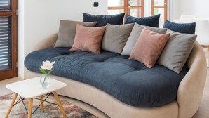 A modern living room with a curved sofa, a small white table, and a vase with a flower. - Casa A&E - Panoramic Lake Orta Views (Prà della Marta)