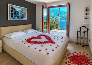 A bedroom with a bed, a heart-shaped rose arrangement on the bed, and a balcony with a view.