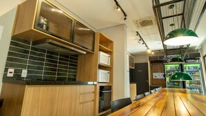 A modern kitchen with wooden cabinets, a black tiled backsplash, and a wooden dining table. - W Be Perdizes (São Paulo)