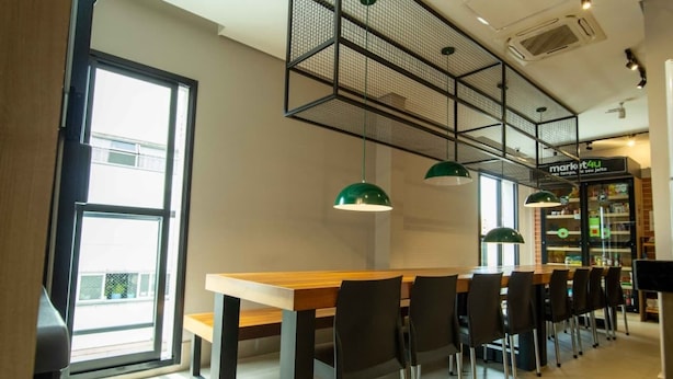 A modern dining area with a long wooden table, black chairs, and green pendant lights. - W Be Perdizes (São Paulo)