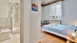 Ett modernt sovrum med en säng, ett litet bord och en stol. Det finns också ett badrum med dusch och toalett.