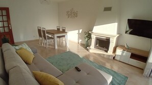Een woonkamer met een bank, een eettafel met stoelen, een open haard en een televisietoestel.