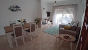 Een woonkamer met een bank, een salontafel, een eettafel met stoelen, een open haard en een televisie.