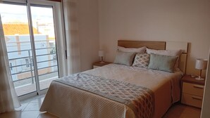 Een slaapkamer met een bed, nachtkastje, lamp en uitzicht buiten via een schuifdeur.